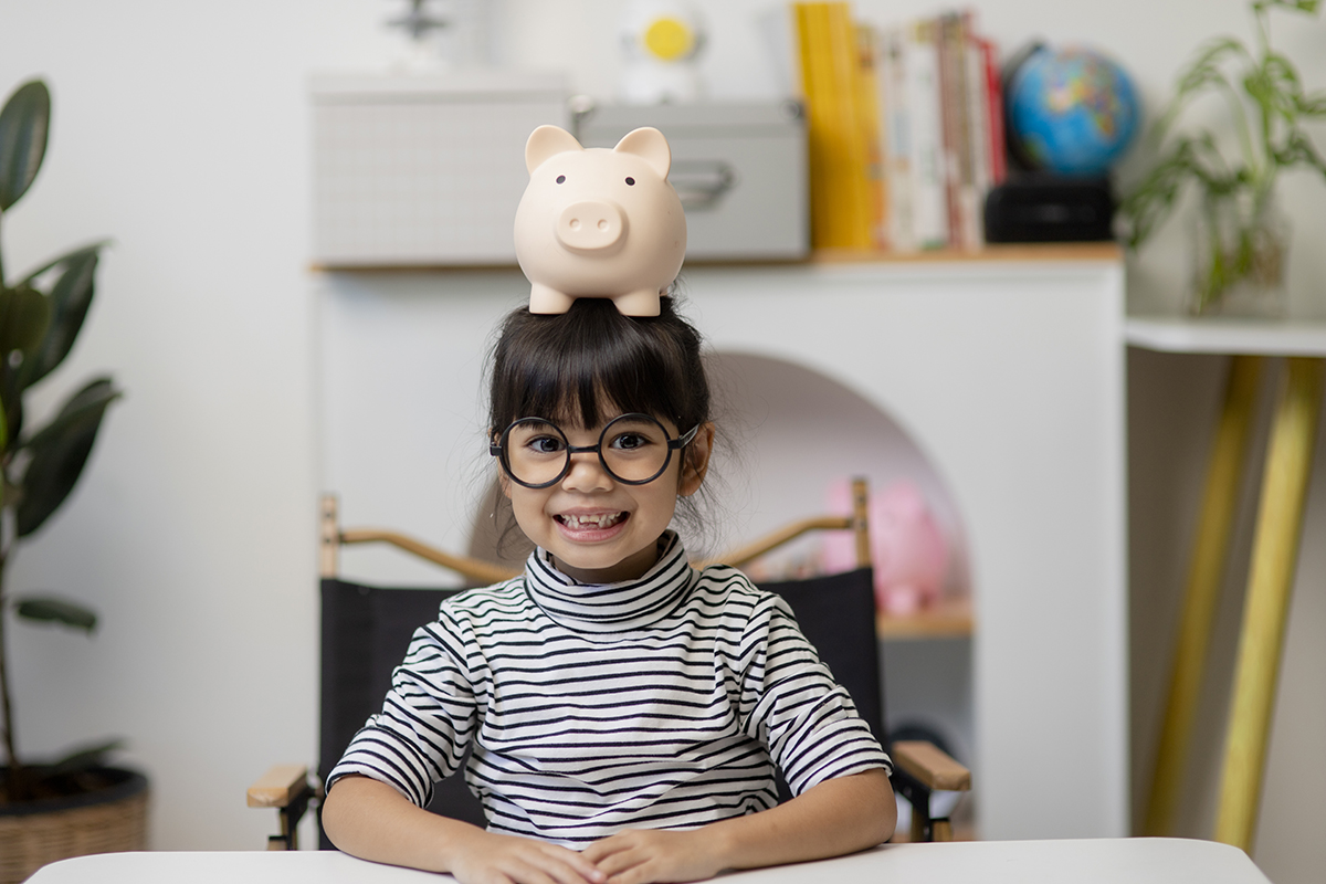 Little girl sitting in living room with piggy bank on her head
