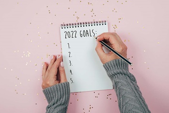 Woman starting to write her 2022 goals on a pad of paper