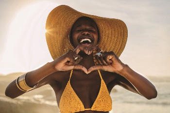 Women in swimsuit on the beach looking very happy and making a heart with her hands