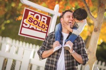 Father and son in front of a house sold sign