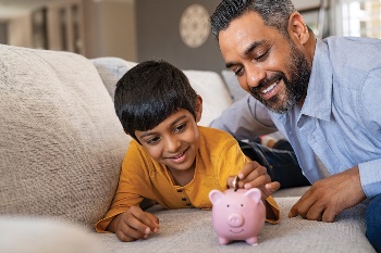 Boy and his dad putting money in a piggy bank