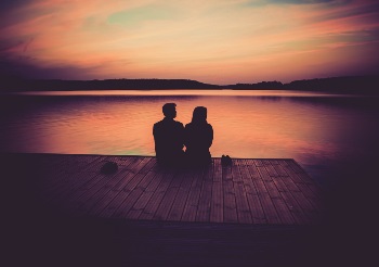 Man and women sitting on a dock looking out onto a sunset