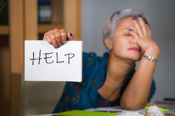 Woman looking overwhelmed holding up a sign that says "help"