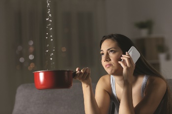 Women on the phone holding a pan that water is dripping into from her ceiling